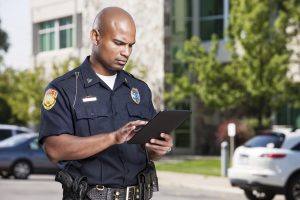 A mid-adult male african american law enforcement officer uses a modern electronic touch screen tablet to enter a citiation or look up information while outdoors.